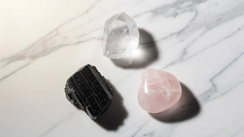 Composition minimaliste de trois pierres thérapeutiques : une tourmaline noire, un cristal de roche et un quartz rose, sur un fond neutre.